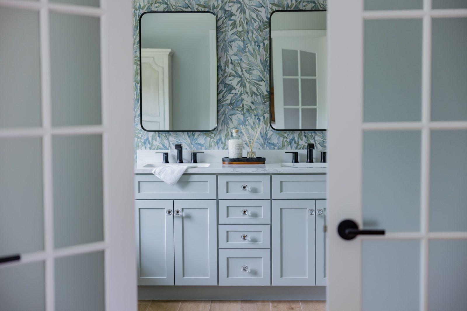 Bathroom vanity with dual mirrors, white cabinetry, and patterned wallpaper by Design House Interiors