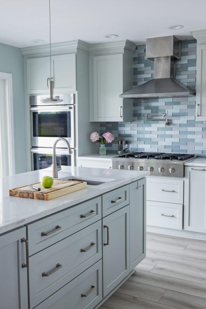 Kitchen cabinetry with light gray finish, metal handles, stainless steel oven, blue tile backsplash, and hardwood floors
