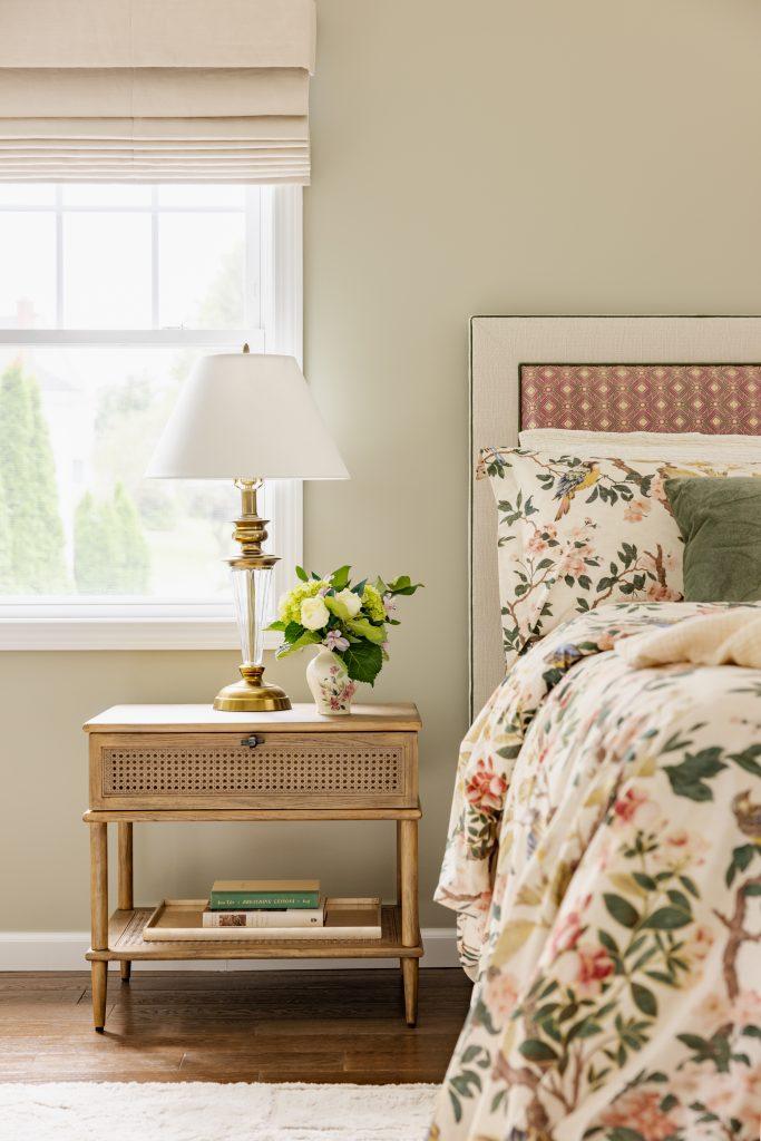 Neutral bedroom with floral bedding, cane nightstand, and brass table lamp by Design House Interiors