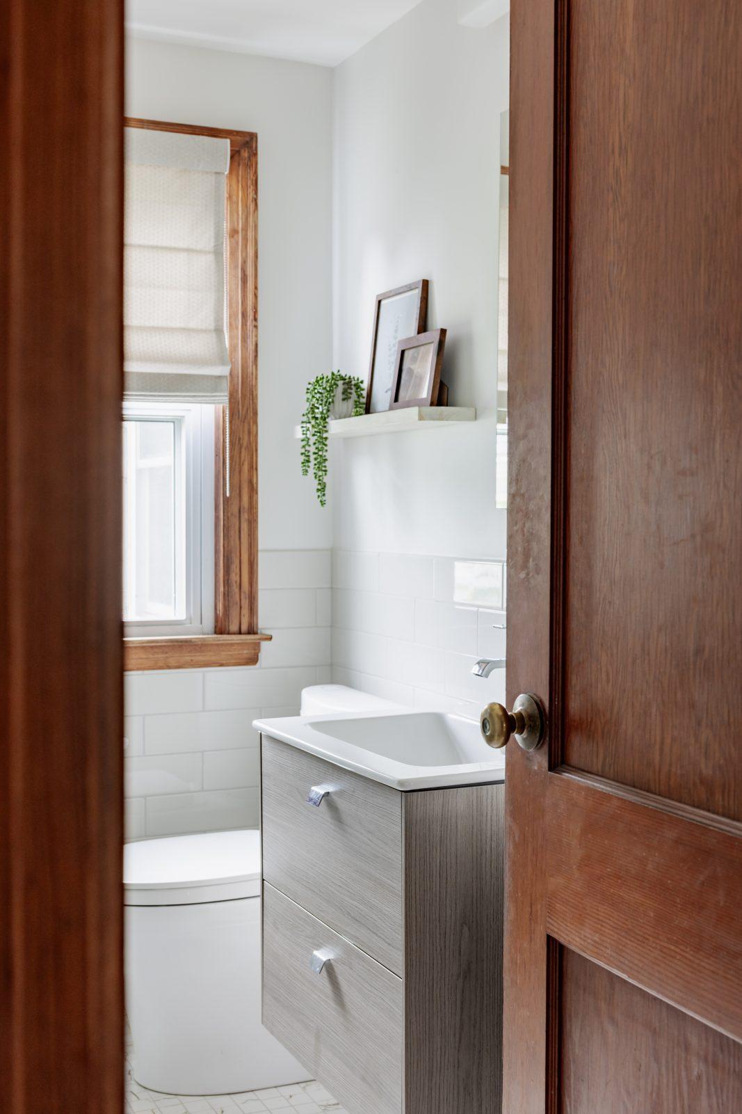 Modern powder room with dark wood door, white floating vanity, and framed mirror by Design House Interiors
