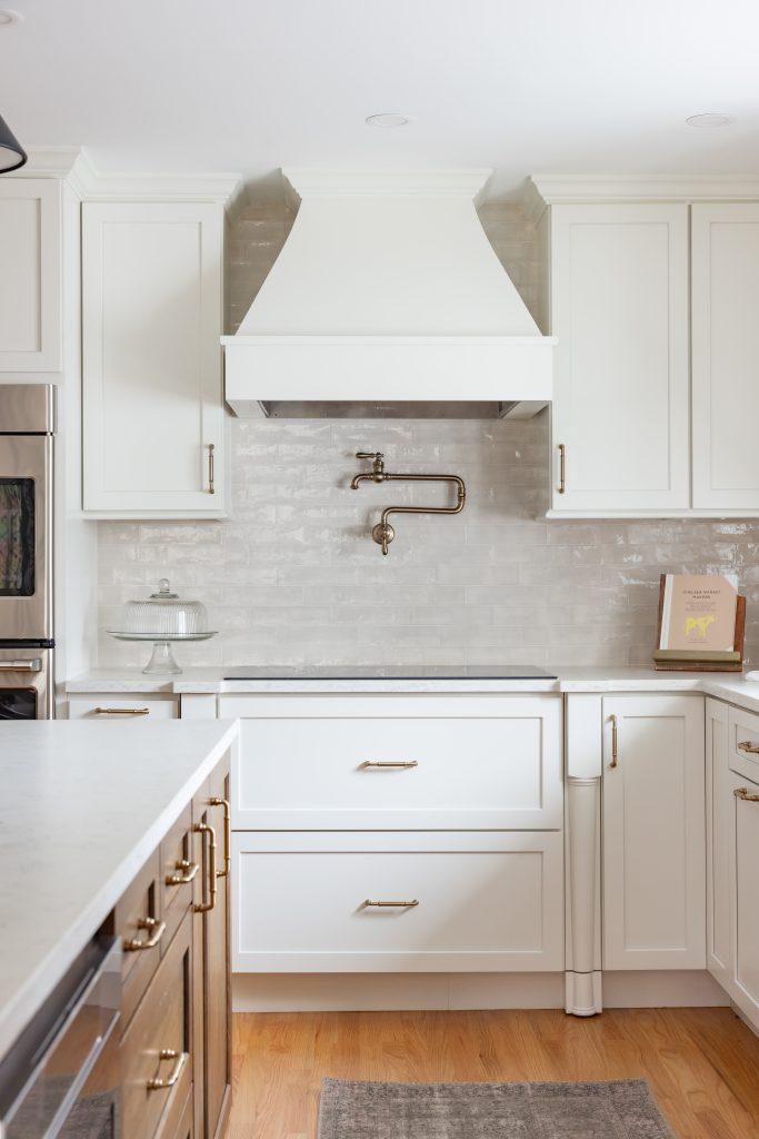 Kitchen with white cabinetry, marble backsplash, and brass hardware by Design House Interiors