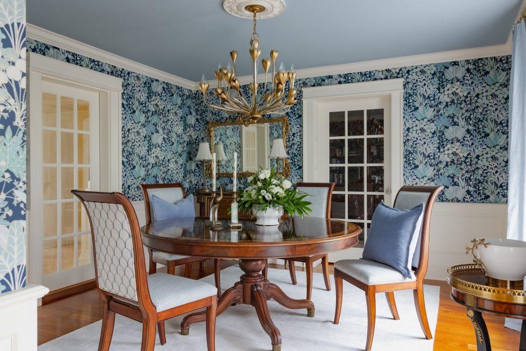 Formal dining room with blue floral wallpaper, gold tulip chandelier, painted ceiling, and oval wood table by Design House Interiors