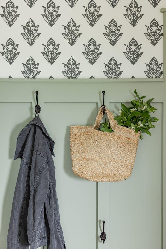 Sage green mudroom wall with black iron hooks and botanical wallpaper by Design House Interior