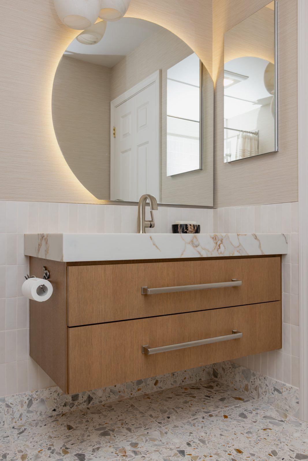 Floating wood vanity with marble countertop and backlit round mirror by Design House Interiors